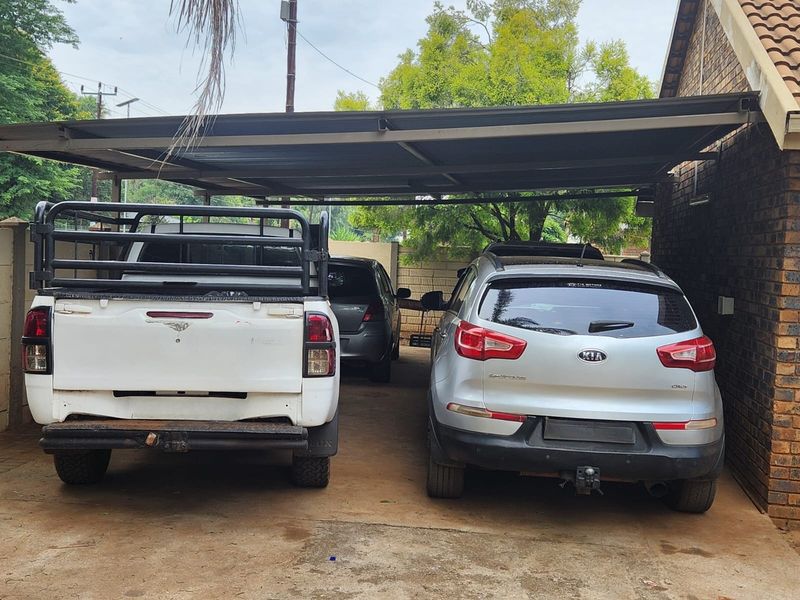 A covered carport area with a concrete driveway and brick wall siding, providing sheltered parking space.