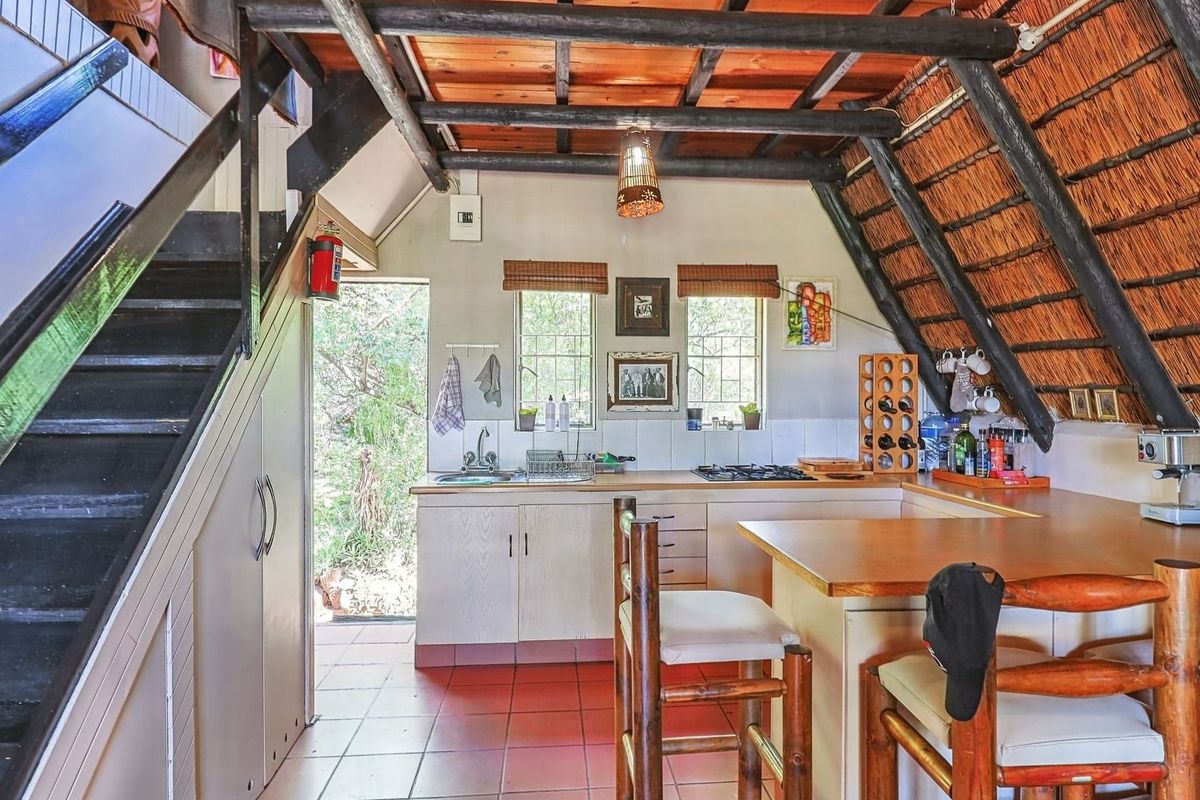 Rustic kitchen featuring exposed timber beams, a thatched ceiling, built-in cabinetry, and a breakfast bar, with direct access to the exterior.