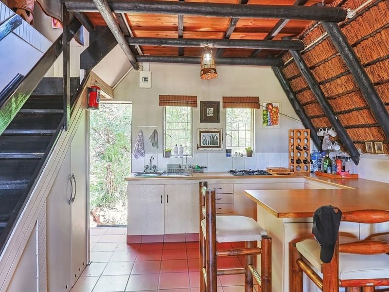 Rustic kitchen featuring exposed timber beams, a thatched ceiling, built-in cabinetry, and a breakfast bar, with direct access to the exterior.