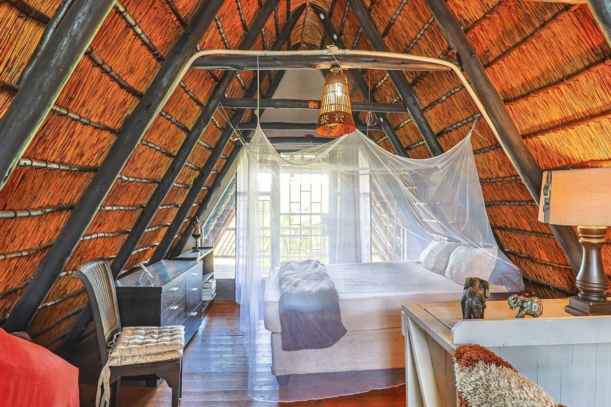 A unique bedroom featuring a high-pitched thatched roof with exposed timber rafters and warm wooden flooring, creating a rustic and cozy atmosphere.