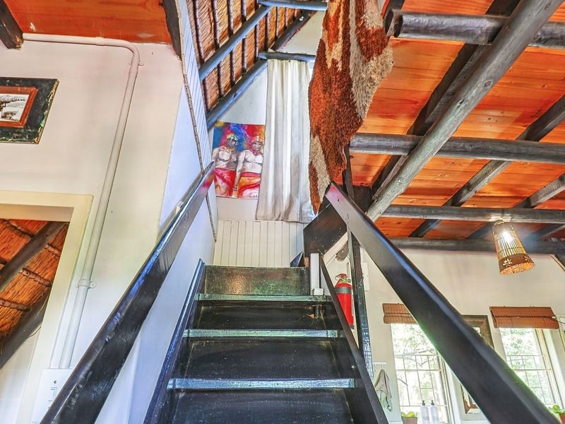 A rustic interior staircase featuring exposed timber rafters, a thatched roof ceiling, and a painted timber staircase with a handrail.