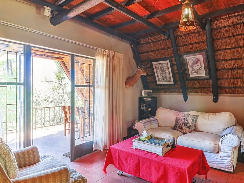 Cozy living room featuring exposed timber beams, a traditional thatched ceiling, tiled floors, and direct access to an outdoor balcony through sliding glass doors.