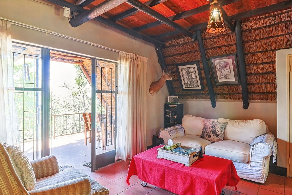 Cozy living room featuring exposed timber beams, a traditional thatched ceiling, tiled floors, and direct access to an outdoor balcony through sliding glass doors.
