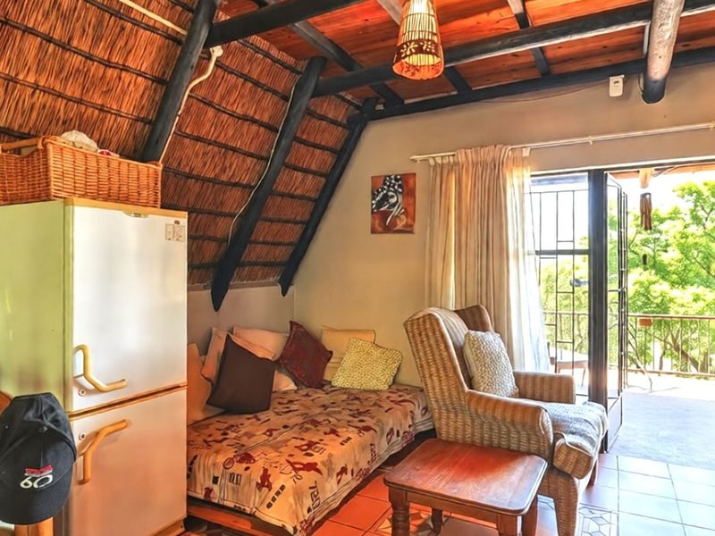 Living area featuring a rustic thatched roof with exposed timber rafters, tiled flooring, and direct access to an outdoor balcony through sliding glass doors.
