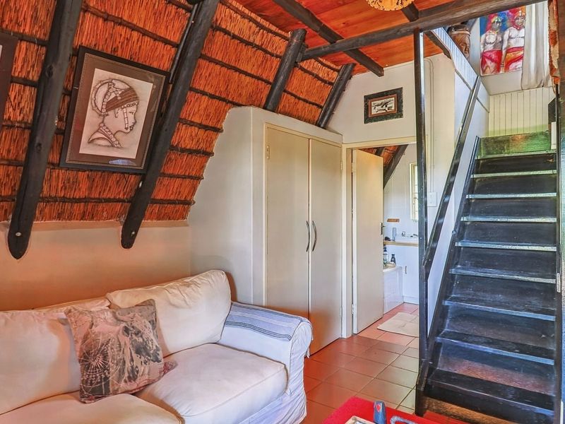 Open-plan living area featuring a unique thatched roof with exposed timber rafters, a staircase leading to the upper level, and an adjacent kitchen area.