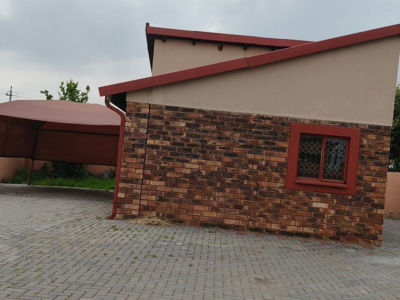Rear exterior view of the property featuring a brick facade, paved driveway, and a shade cloth carport structure.
