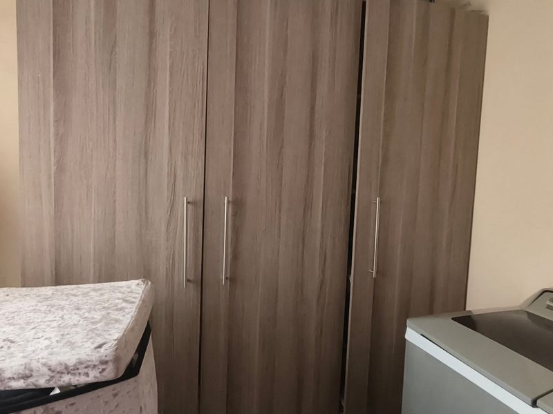 A bedroom featuring a large, modern wood-finish built-in wardrobe with vertical metal handles.