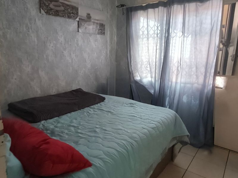 A compact bedroom featuring tiled flooring and a window fitted with a security gate, requiring cosmetic updates to improve its overall condition.