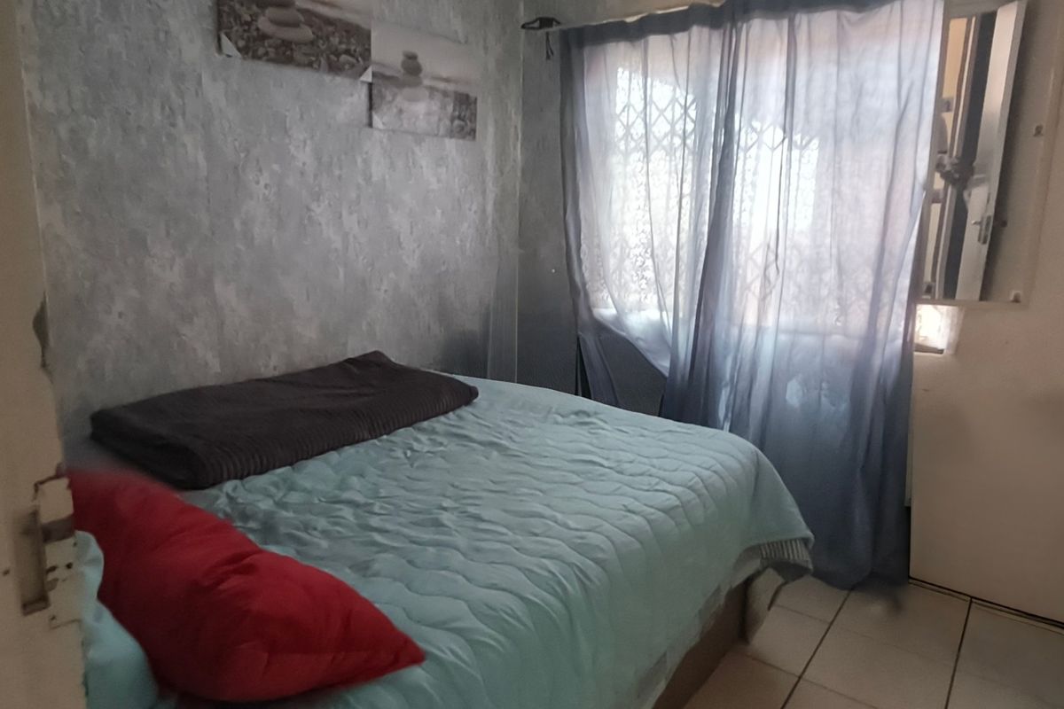 A compact bedroom featuring tiled flooring and a window fitted with a security gate, requiring cosmetic updates to improve its overall condition.