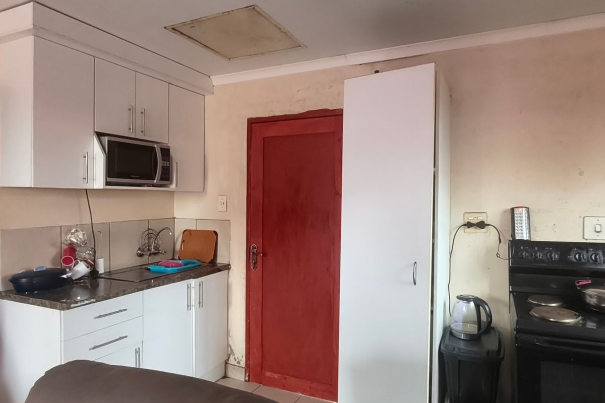 Compact kitchen featuring white cabinetry, laminate countertops, built-in microwave, and an electric stove, requiring cosmetic updates to improve overall condition.