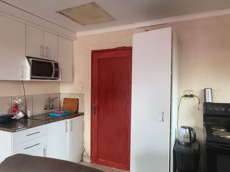 Compact kitchen featuring white cabinetry, laminate countertops, built-in microwave, and an electric stove, requiring cosmetic updates to improve overall condition.
