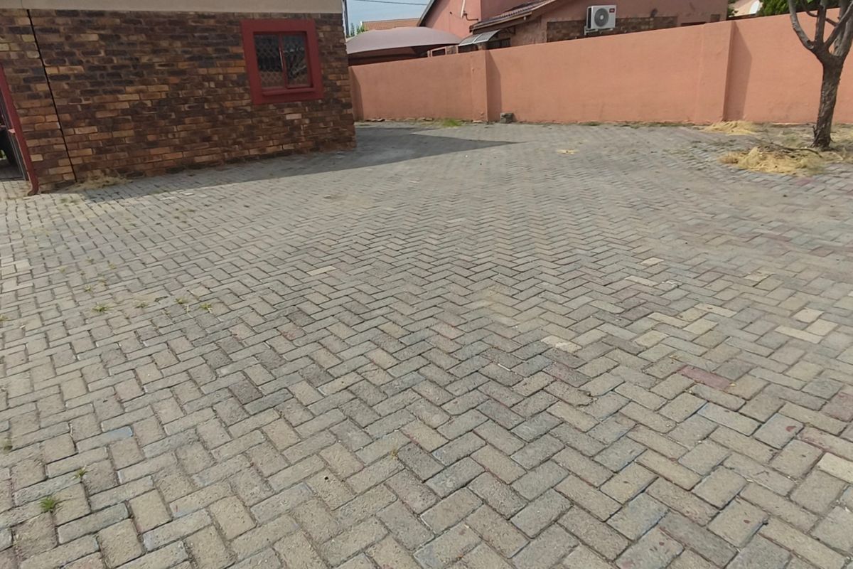 A paved rear courtyard area featuring face brick walling, a perimeter boundary wall, and an external air conditioning unit.