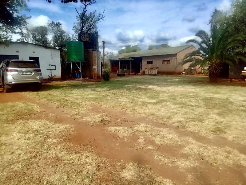 Rear view of the farm property featuring an outbuilding, water storage tank, and open yard space with established landscaping.