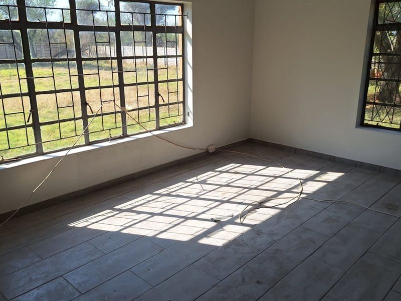 An empty bedroom featuring tiled flooring and large windows with metal security bars, offering a bright and open space ready for customization.