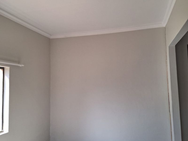A clean, empty bedroom featuring neutral wall paint, crown molding, and tiled flooring, providing a blank canvas for personalization.