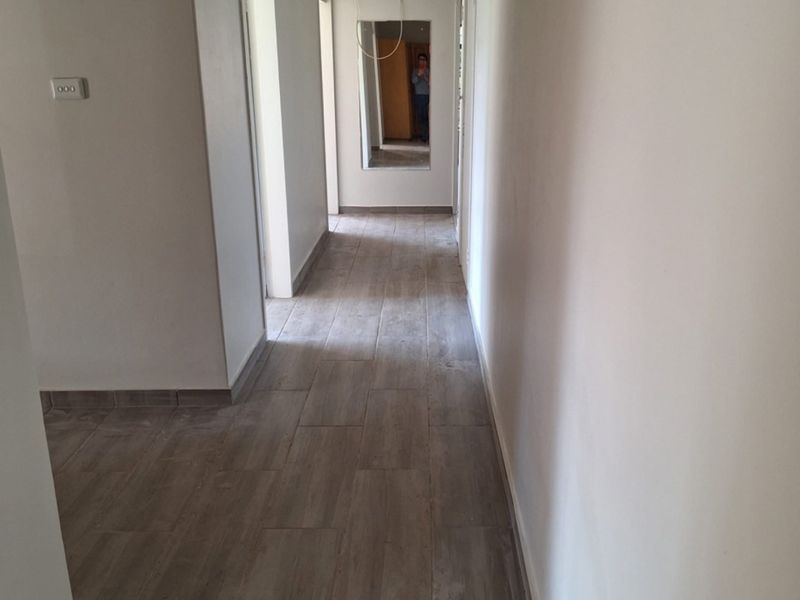 A clean, empty hallway featuring neutral tiled flooring and white walls, providing a bright and functional transition space within the home.