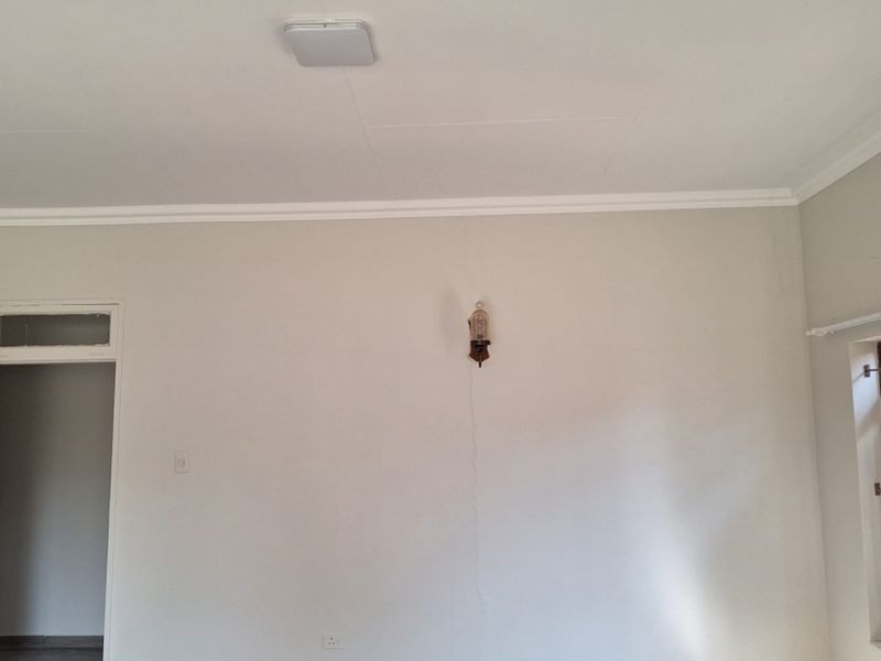 An empty living room featuring neutral walls, tiled flooring, coving, and a wall sconce, providing a blank canvas for interior design.