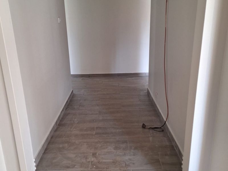 A vacant hallway featuring neutral wall finishes and modern wood-look tiled flooring, providing a clean and simple transition space.