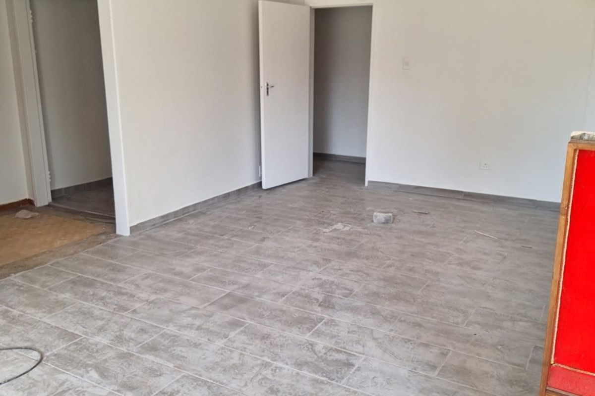 A bright, empty living area featuring modern grey tiled flooring, neutral walls, and internal doors with transom windows.
