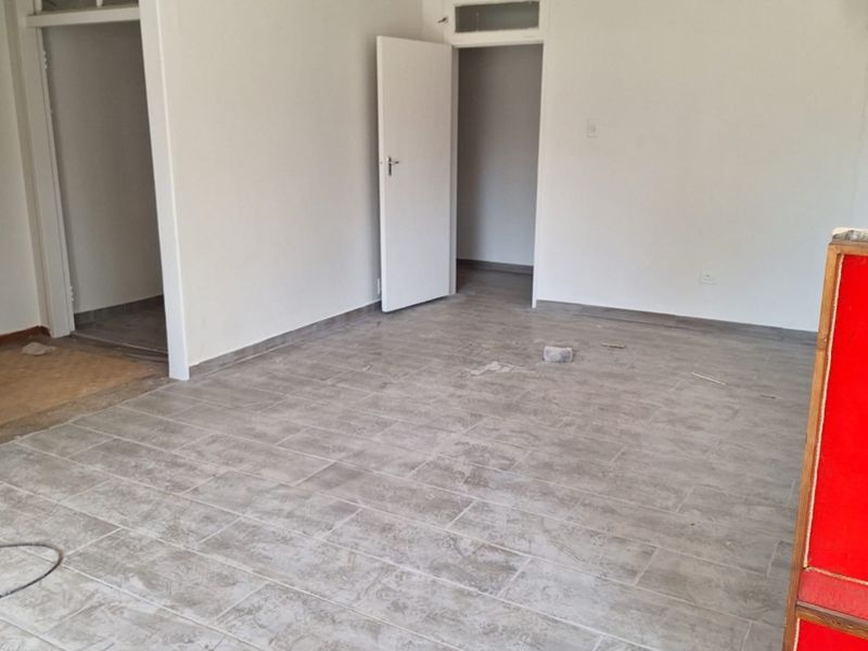 A bright, empty living area featuring modern grey tiled flooring, neutral walls, and internal doors with transom windows.