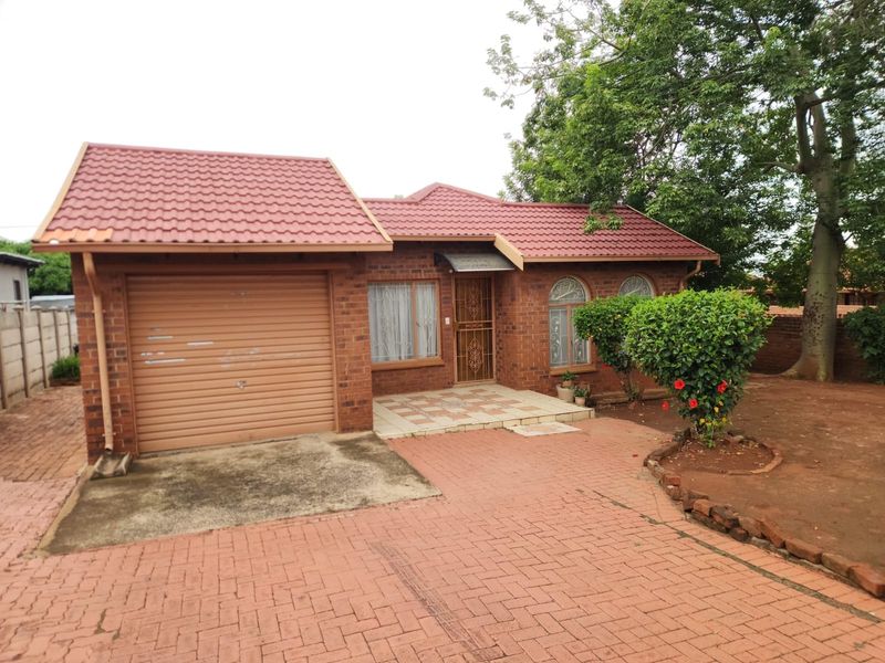 Front view of a single-story brick house featuring a tiled roof, an integrated garage with a roller door, and a paved driveway.