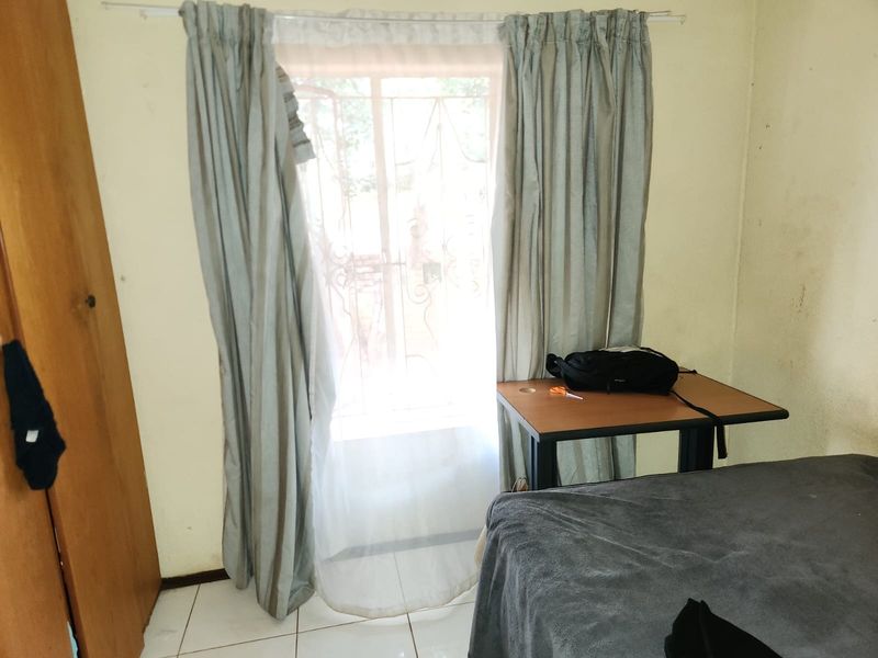 A bedroom featuring tiled flooring, a built-in wardrobe, and a window fitted with a security gate.