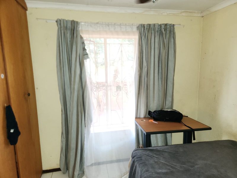 A bedroom featuring tiled flooring, a ceiling fan, and a security gate over the window, showing signs of wear and ceiling water damage.