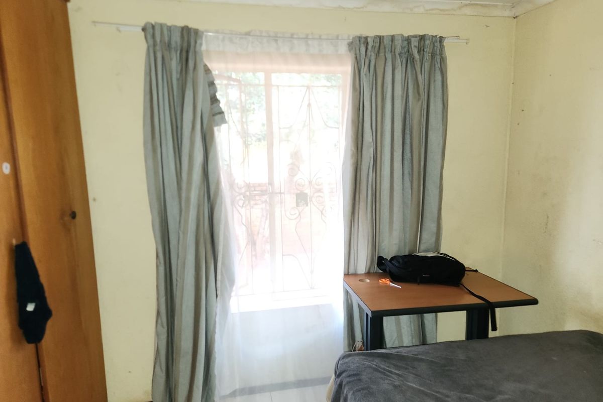 A bedroom featuring tiled flooring, a ceiling fan, and a security gate over the window, showing signs of wear and ceiling water damage.