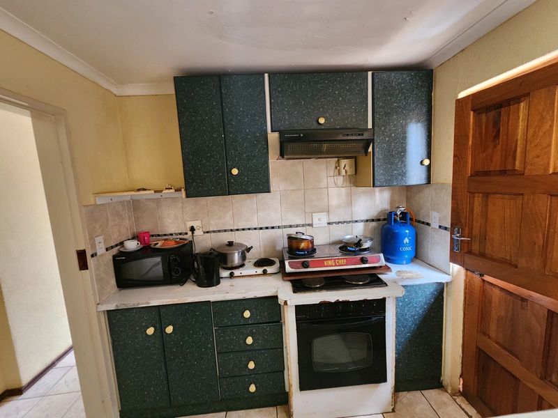 A compact kitchen featuring dark green cabinetry, a tiled backsplash, and a built-in oven with a gas hob setup.