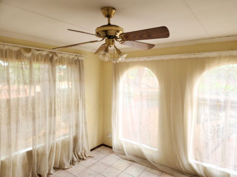 A bright, empty living area featuring tiled flooring, a ceiling fan, and distinctive arched windows with security bars.