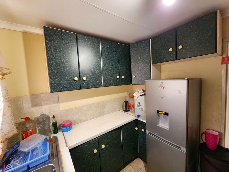 A compact kitchen featuring dark green laminate cabinetry, a tiled backsplash, and a stainless steel sink, offering a functional but dated layout.