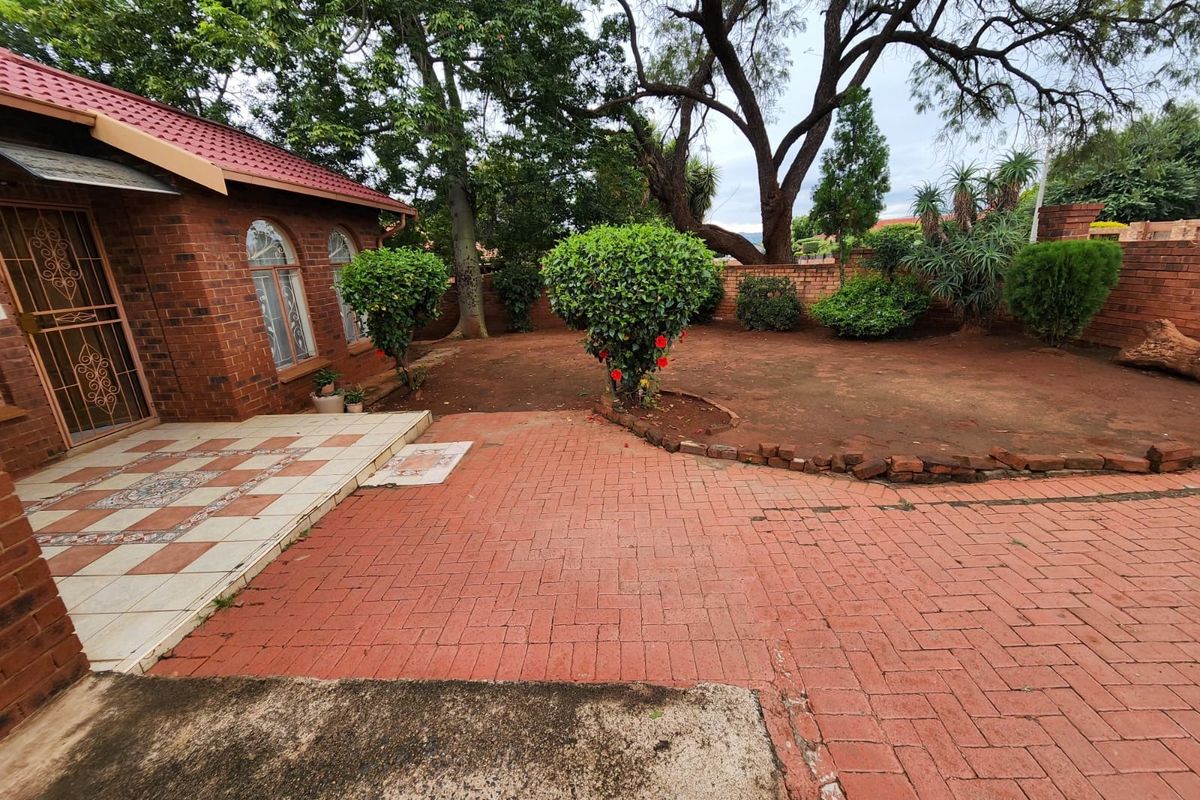Rear exterior view featuring a brick facade, tiled patio area, and paved courtyard leading to a garden with a brick boundary wall.