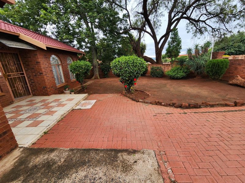 Rear exterior view featuring a brick facade, tiled patio area, and paved courtyard leading to a garden with a brick boundary wall.