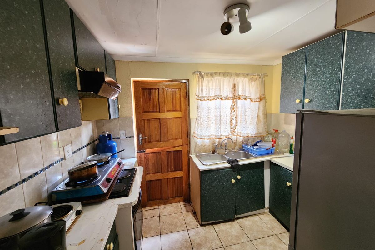 A functional kitchen featuring laminate cabinetry, a double bowl sink, tiled backsplash, and tiled flooring, with a timber door leading to the exterior.