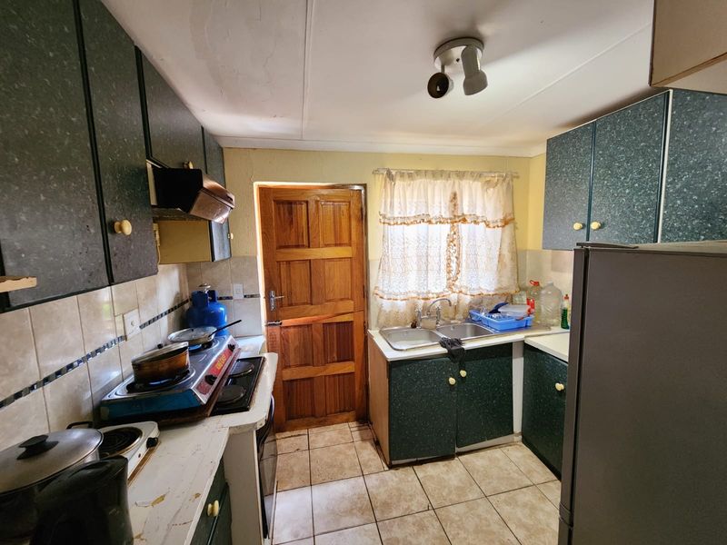 A functional kitchen featuring laminate cabinetry, a double bowl sink, tiled backsplash, and tiled flooring, with a timber door leading to the exterior.