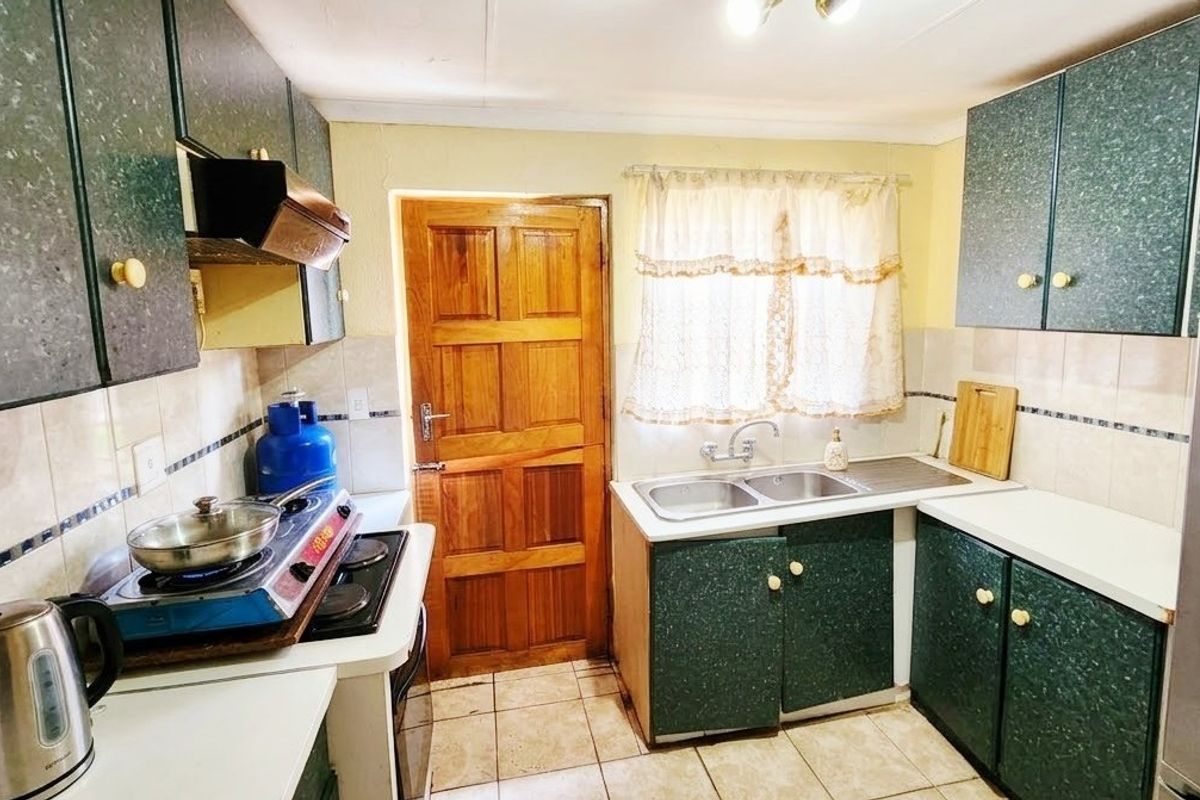 A functional kitchen featuring laminate cabinetry, a double basin sink, tiled backsplash, and tiled flooring with direct access to an exterior timber door.
