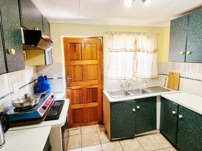 A functional kitchen featuring laminate cabinetry, a double basin sink, tiled backsplash, and tiled flooring with direct access to an exterior timber door.