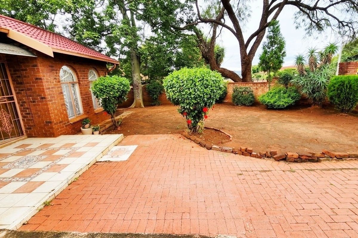 A rear exterior view featuring a brick-paved patio, tiled entrance area, and a garden space enclosed by a brick boundary wall.