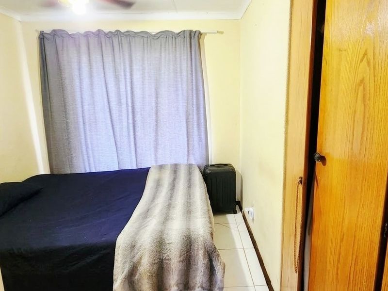 A functional bedroom featuring tiled flooring, a ceiling fan, and a built-in wooden wardrobe.