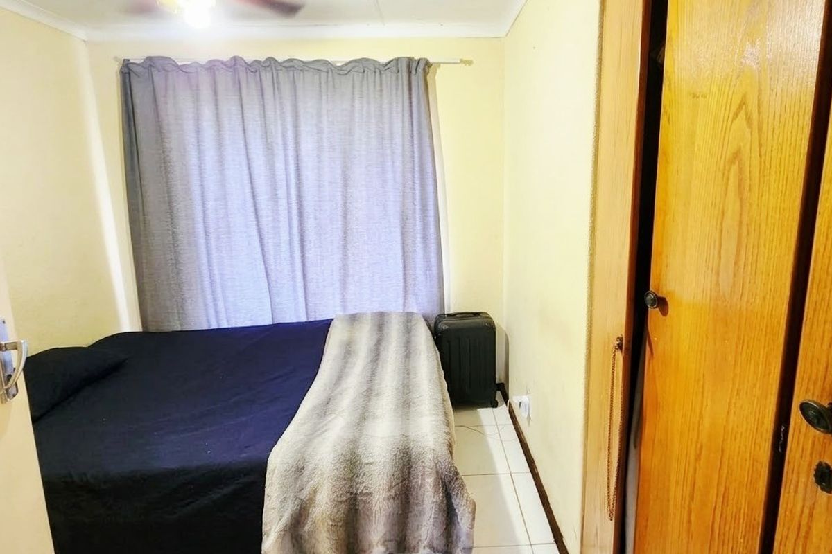 A functional bedroom featuring tiled flooring, a ceiling fan, and a built-in wooden wardrobe.