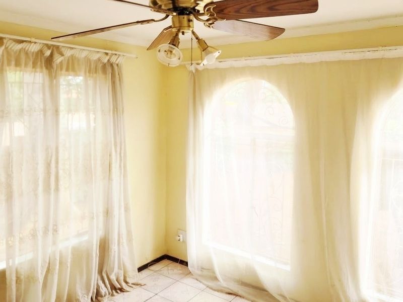A bright, empty living area featuring tiled flooring, a ceiling fan, and distinctive arched windows that allow for ample natural light.