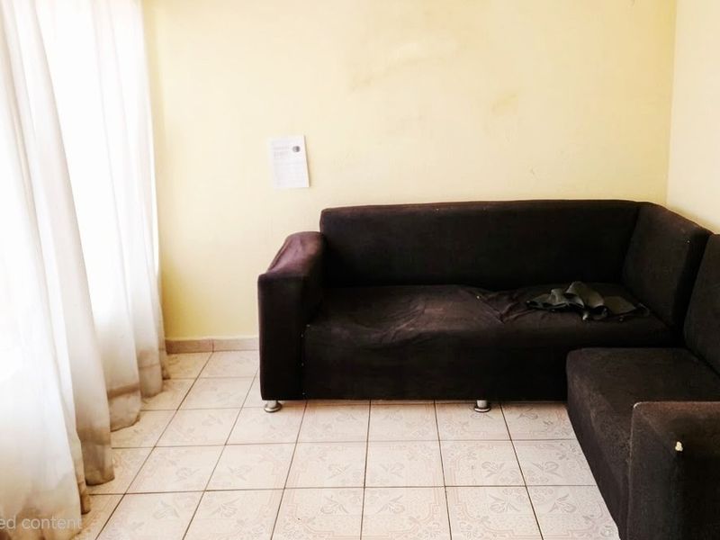 A living room area featuring ceramic floor tiles and plain walls, currently requiring cosmetic updates and fresh paint to improve the overall aesthetic.