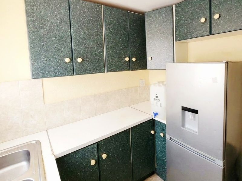 A compact kitchen featuring dated green laminate cabinetry, white countertops, a stainless steel sink, and a tiled backsplash.