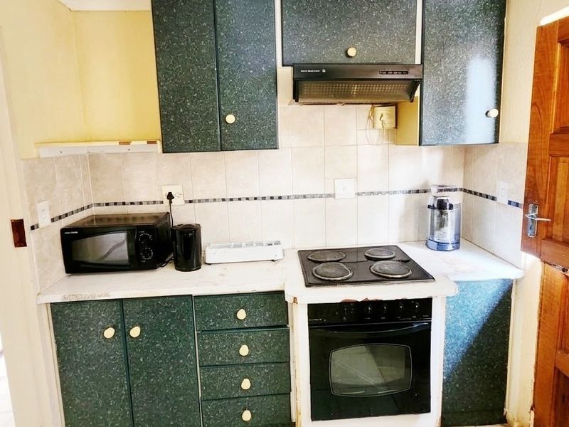A compact kitchen featuring dark green cabinetry, a built-in oven with electric hob, extractor fan, and tiled backsplash.