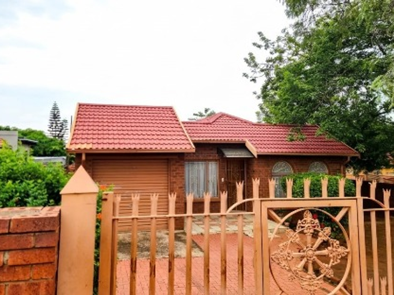 Front view of a face brick house featuring a tiled roof, integrated garage, and secure metal fencing with a paved driveway.