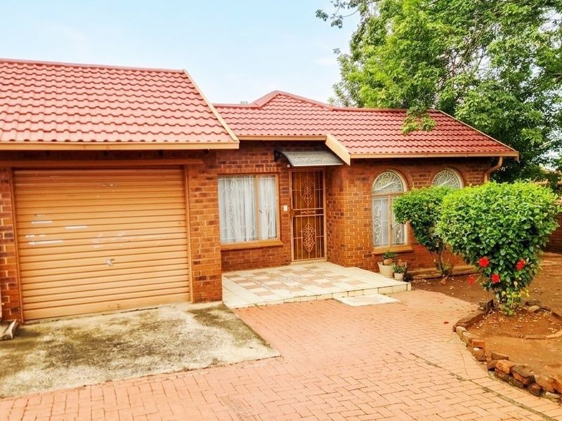 A single-story face brick house featuring a tiled roof, an integrated roll-up garage, and a paved front entrance area.
