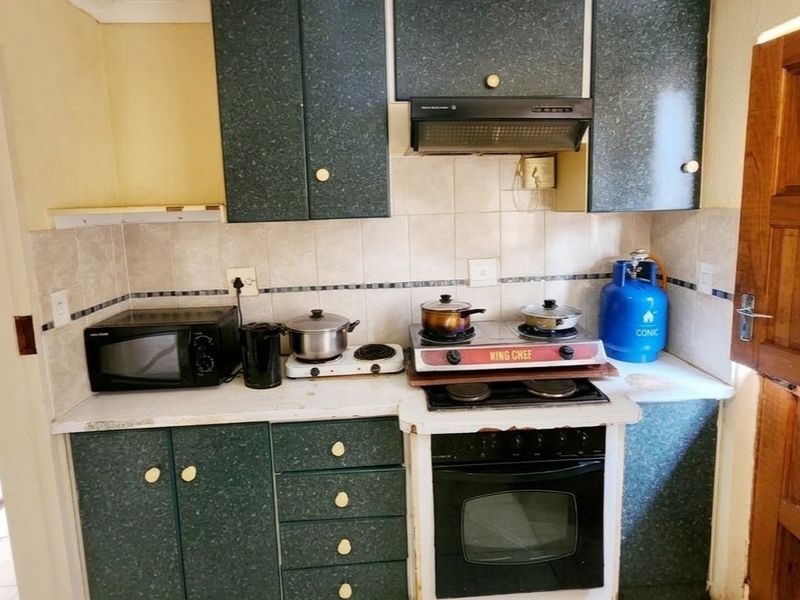 A compact kitchen featuring dated dark green cabinetry, tiled backsplash, built-in oven, and extractor fan, offering potential for a modern renovation.