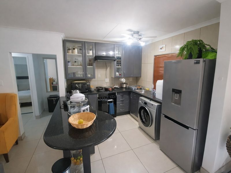 Open-plan kitchen featuring modern grey cabinetry, granite countertops, a breakfast bar, and integrated stainless steel appliances, seamlessly connected to the living area.
