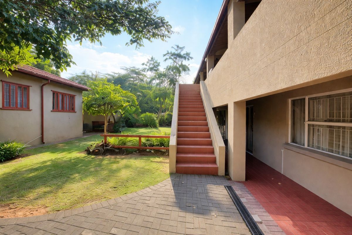 Rear exterior view of the apartment building featuring a tiled staircase, paved walkway, and access to a shared garden area.