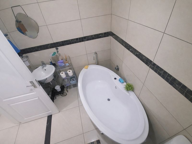 A compact bathroom featuring a modern freestanding bathtub, wall-mounted basin, and neutral ceramic tiling with a decorative mosaic accent border.